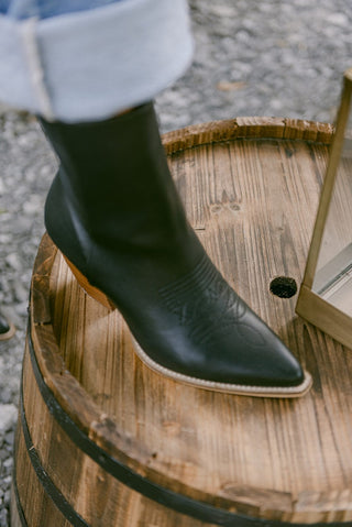 black vegan leather booties with a pointed toe and a low wooden heel,  side zip closure and embedded cowgirl boot design, top view