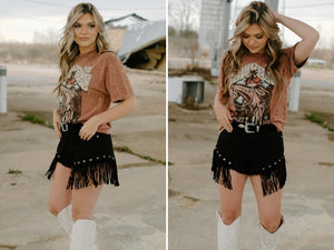 rust burgundy mineral wash western short sleeve crew neck graphic tee with black denim fray fringe shorts and bone knee high cowgirl boots 