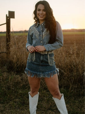medium wash rhinestone fringe long sleeve collared button up cropped denim jacket with medium wash high waisted rhinestone fringe hem denim mini skirt and white rhinestone cowgirl boots