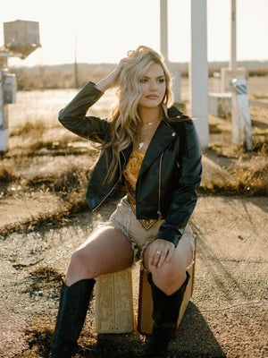 black faux leather fringe long sleeve jacket with golden yellow satin bandana sleeveless crop top and taupe high waisted rhinestone fringe denim shorts