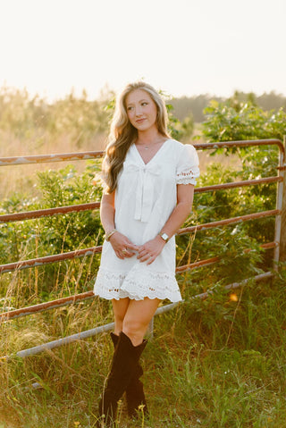 White V-neck bow dress with puff sleeves and lace trim detailing.