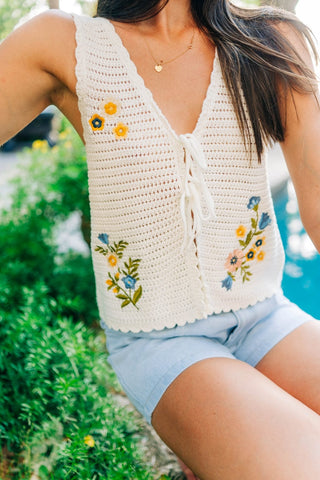 White top with colorful embroidered floral details. Open in front with two ties that are adjustable. Sizes small-large 