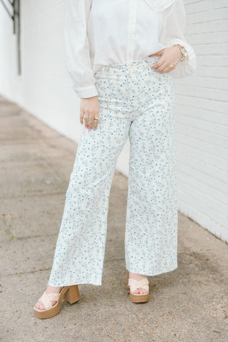 White wide leg jeans with blue floral detailing and raw hem.