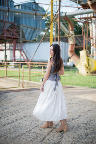 Woman in a white flowy skirt standing in an industrial area with large machines and structures.