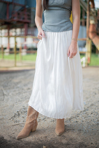 Person wearing a white long flowy skirt and brown cowgirl boots on a blurred outdoor background