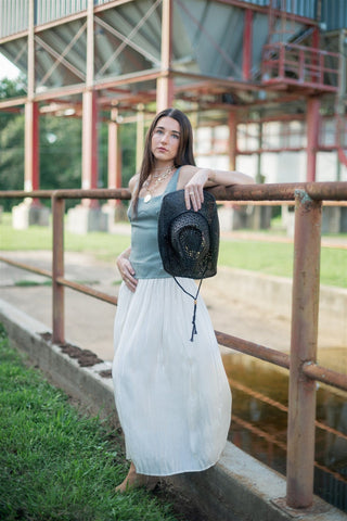 Woman in a long dress and hat leaning against a metal railing with a barn in the background