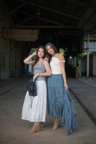 Two women posing together in an industrial setting wearing long skirts and cowgirl boots