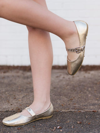 Mary Jane flats featuring a gold metallic finish and an adjustable buckle strap with a rounded toe