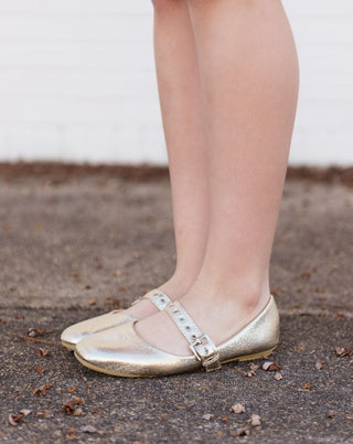 Mary Jane flats featuring a gold metallic finish and an adjustable buckle strap with a rounded toe, side view