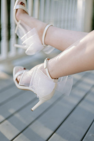 white sparkling, shimmery heels with a square toe design and a delicate ankle strap with unique bow back detail, bow detail view